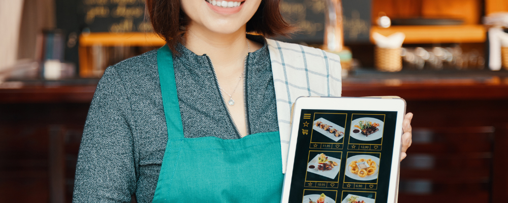 A woman holding her POS system for her Japanese restaurant with pictures of food.