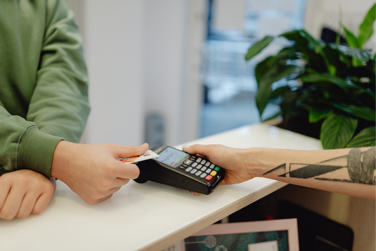 a customer's hand offering their credit card to a cashier at a the point of sale to use a card reader