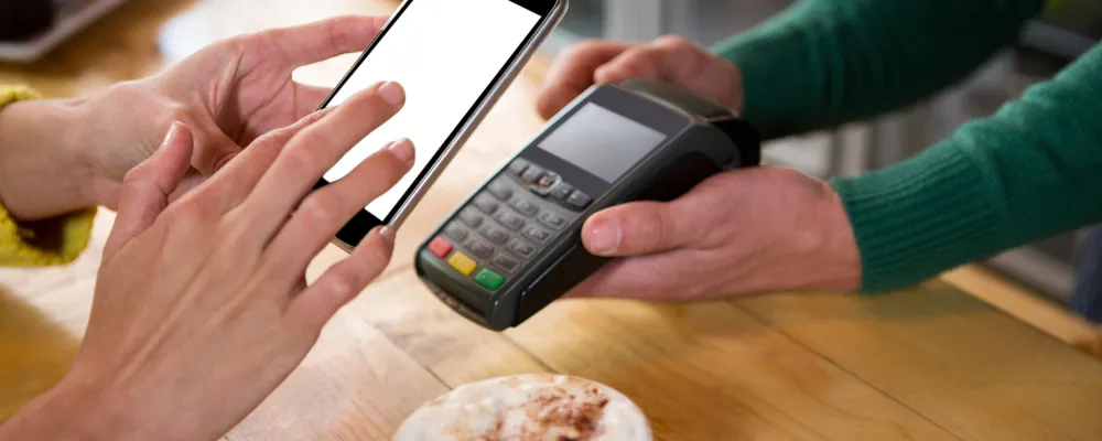 Two people, faces out of frame, hands in frame, using a phone and a POS terminal to verify a link payment.