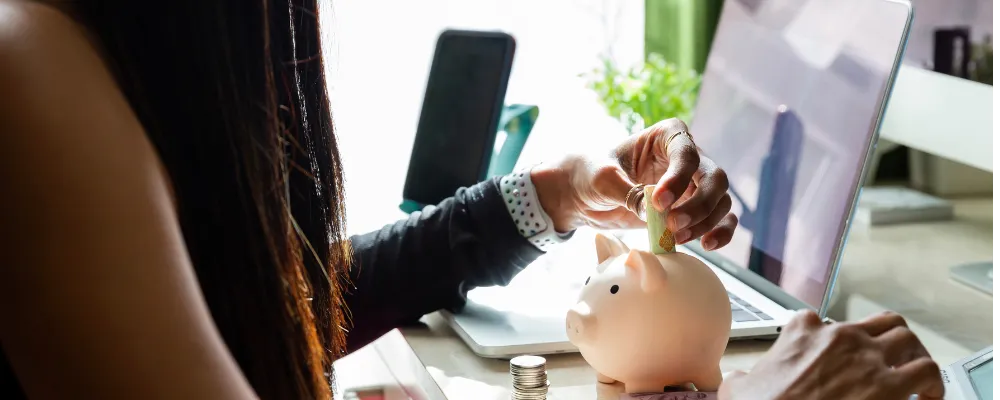 A woman sitting at a laptop in front of piggy bank and coins, researching PCI compliance.