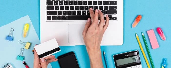 a business owner's hand on a laptop keyboard researching what is merchant account against a blue background