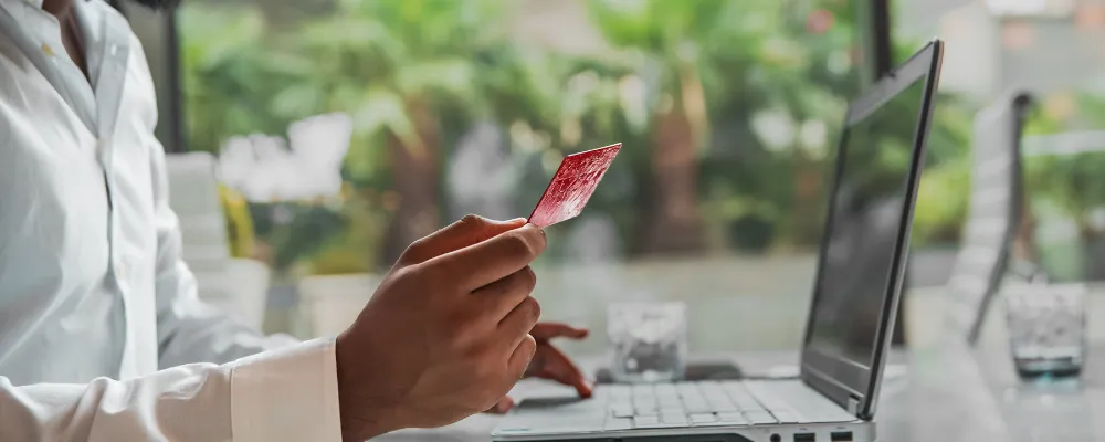 Someone sitting in front of a computer holding a credit card with their face out of frame while completing an ACH payment.