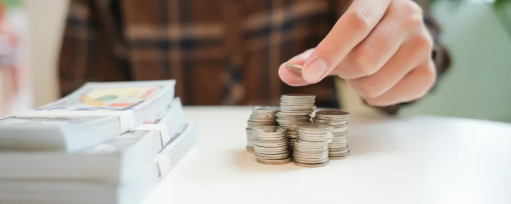 A woman stacking coins and currency, face out of frame, in the process of learning how to become a registered ISO.