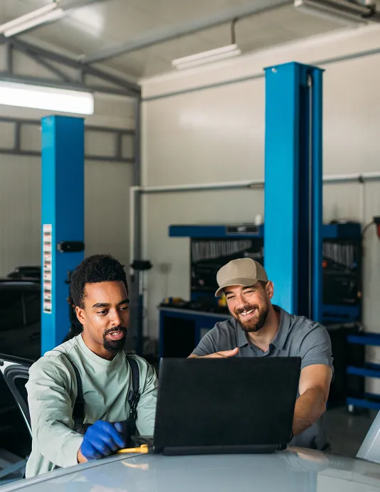An automotive worker and a customer sitting at a table in front of a laptop.
