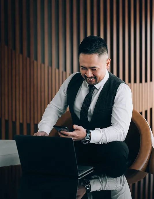 A merchant in front of a laptop with a phone, managing B2B sales.