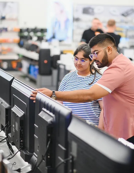 A merchant helping a customer with a row of computer monitors at a store selling electronics and gadgets.