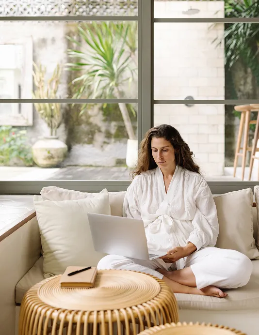 A merchant in a robe on a couch with a laptop, offering health and wellness services.