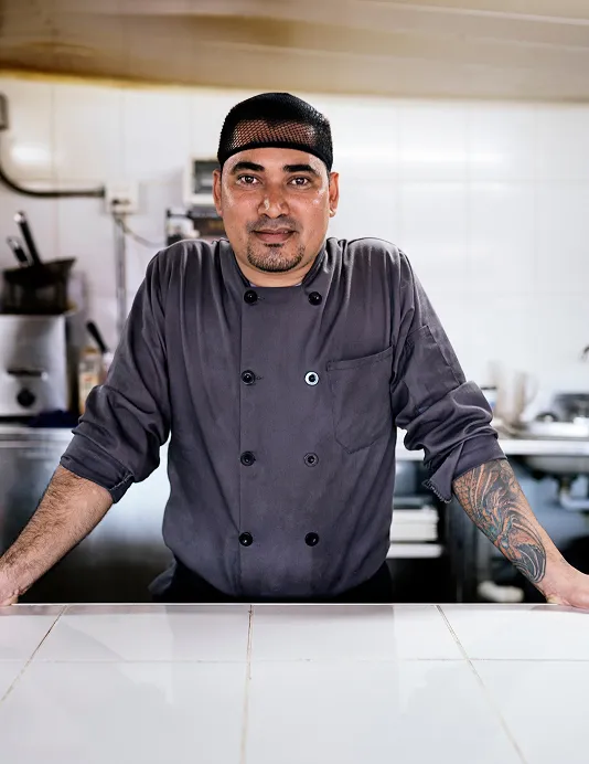 A chef with a hairnet and gray shirt standing at a counter in a restaurant.