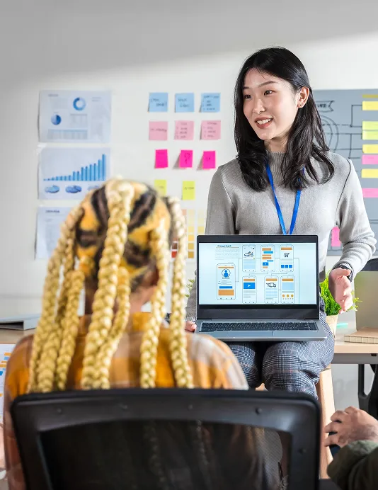 A woman sitting on a desk, her laptop facing a crowd, with SaaS services on the screen.